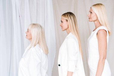side view of elegant three-generation blonde women in total white outfits clipart