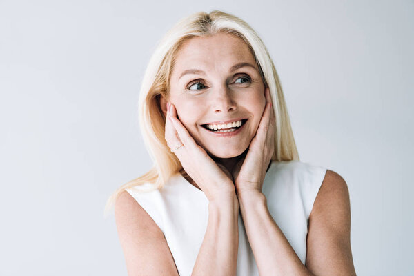 счастливая блондинка зрелая женщина с руками возле лица глядя в сторону изолированы на серый
