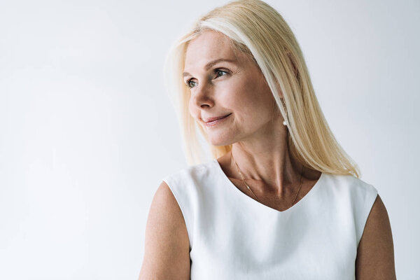 Улыбающаяся блондинка, элегантная зрелая женщина смотрит в сторону, изолированная от серого
