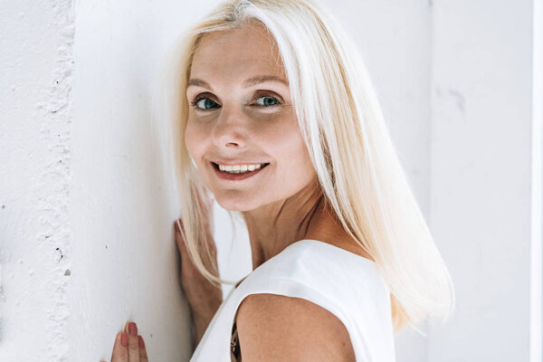 happy blonde mature woman posing near white wall
