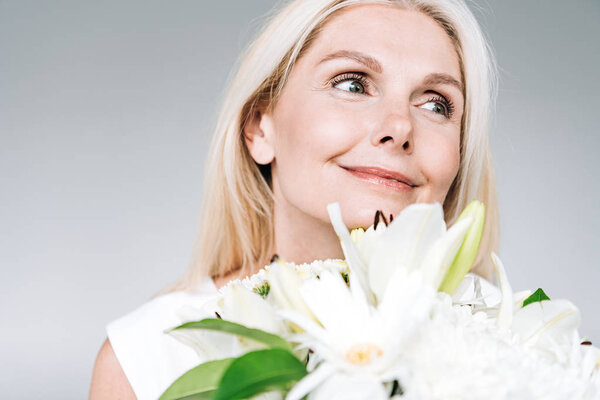 счастливая блондинка зрелого возраста с белыми цветами, уединившись на сером

