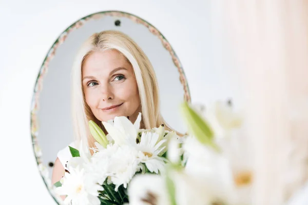 Blonde Rijpe Vrouw Met Bloemen Zoek Door Spiegel Geïsoleerd Wit — Stockfoto