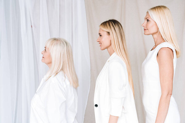 side view of elegant three-generation blonde women in total white outfits