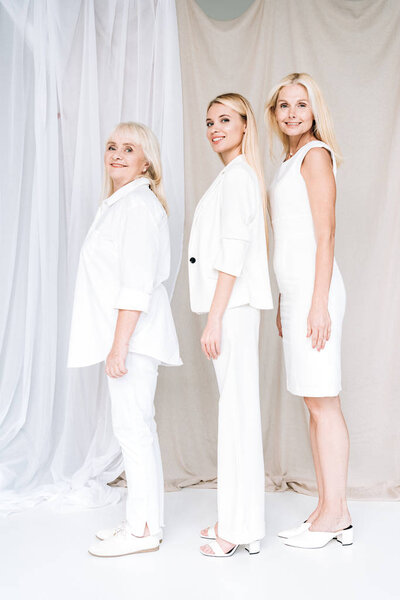 side view of elegant happy three-generation blonde women in total white outfits