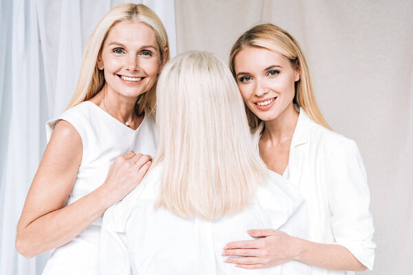 happy mother and daughter in total white outfits near senior woman 