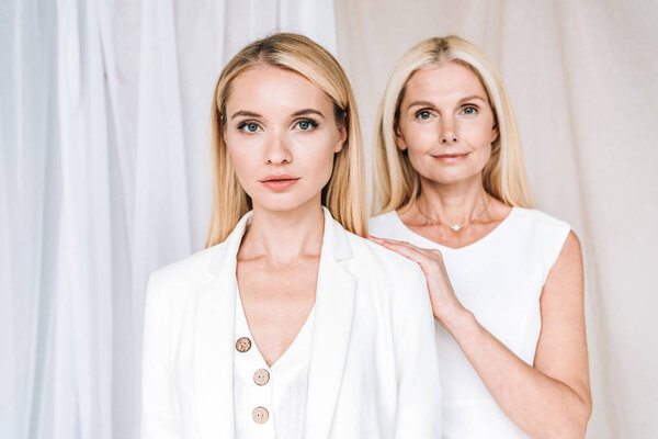 elegant blonde smiling mother and serious daughter in total white outfits