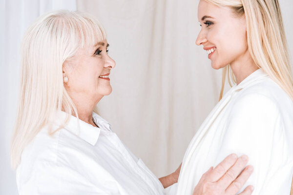 smiling blonde grandmother and granddaughter in total white outfits standing face to face