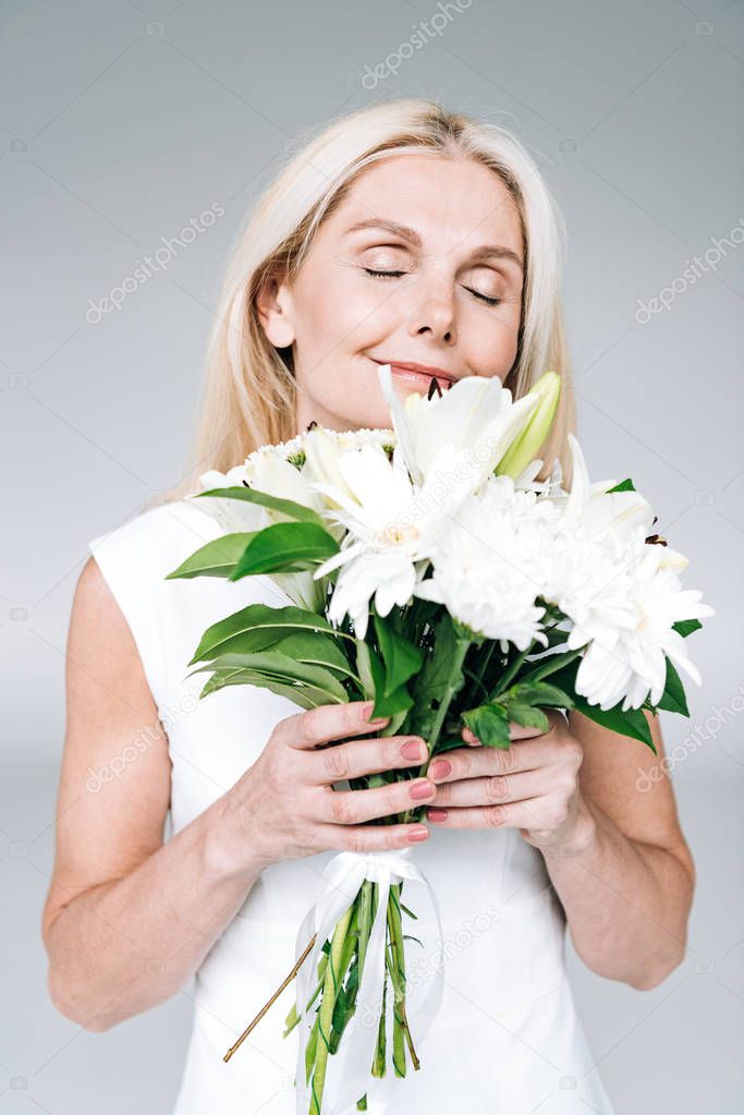 pleased blonde mature woman with white flowers isolated on grey