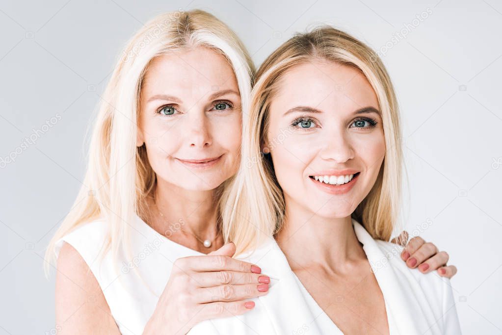 blonde smiling mature mother and adult daughter isolated on grey