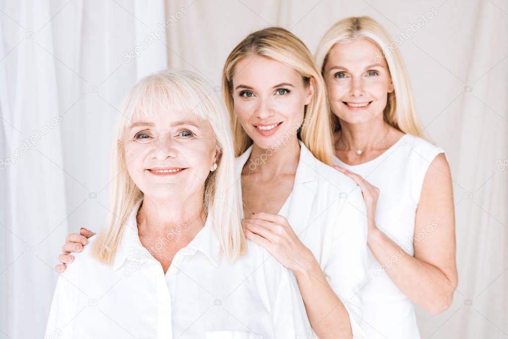 happy elegant three-generation blonde women in total white outfits