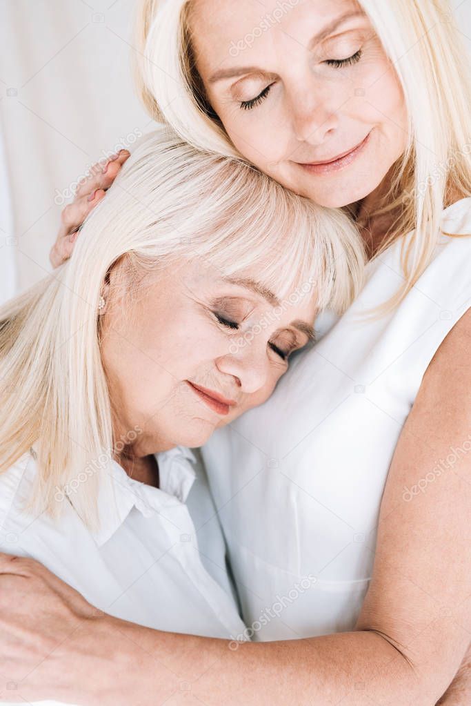 blonde mature daughter and senior mother embracing with closed eyes