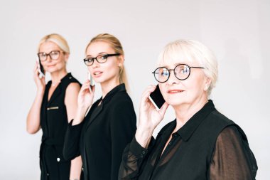 toplam siyah kıyafetler ve gözlük moda üç nesil sarışın iş kadınları gri izole akıllı telefonlar üzerinde konuşurken