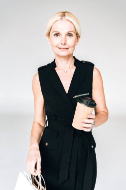 alışveriş çantaları ve kahve ile siyah kıyafetli zarif sarışın kadın gri izole gitmek