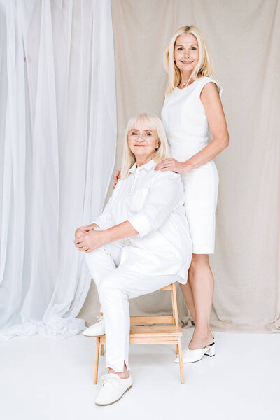 full length view of elegant blonde mature daughter and senior mother in total white outfits