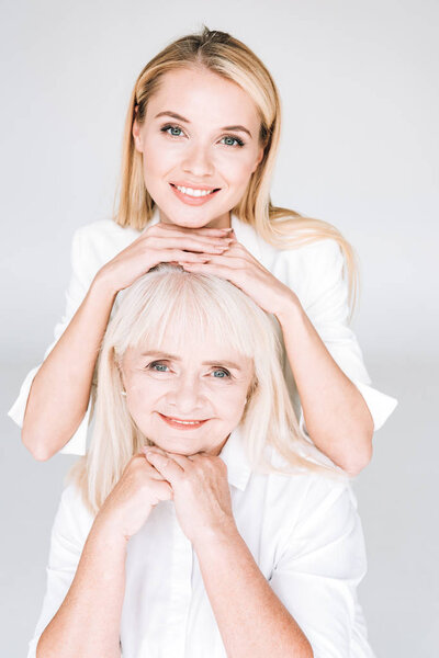 happy blonde grandmother and granddaughter in total white outfits isolated on grey