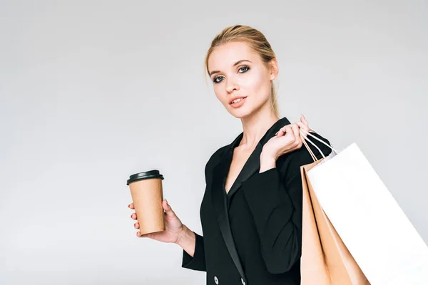 灰色に孤立して行くためにショッピングバッグとコーヒーと黒い衣装でエレガントなブロンドの女性 — ストック写真