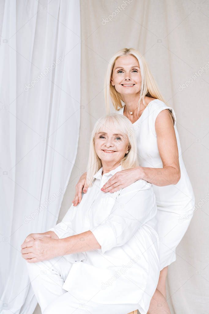 happy blonde mature daughter and senior mother in total white outfits