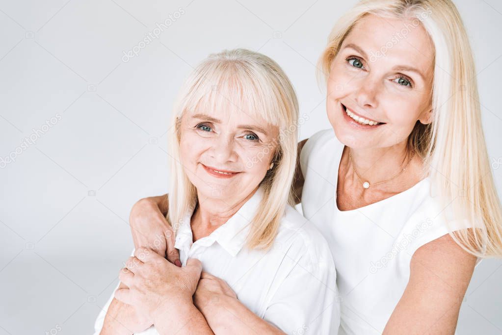 elegant blonde mature daughter and senior mother in total white outfits isolated on grey