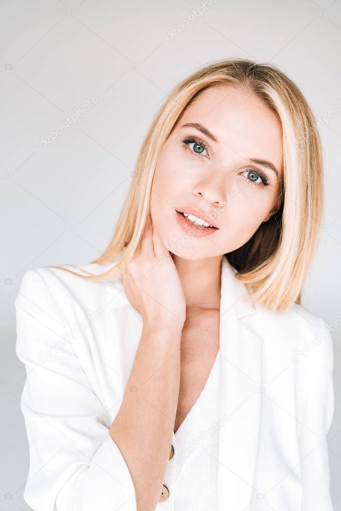 portrait of beautiful young blonde woman in total white outfit isolated on grey