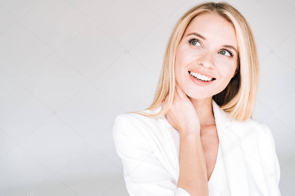 smiling beautiful young blonde woman in total white outfit looking away isolated on grey