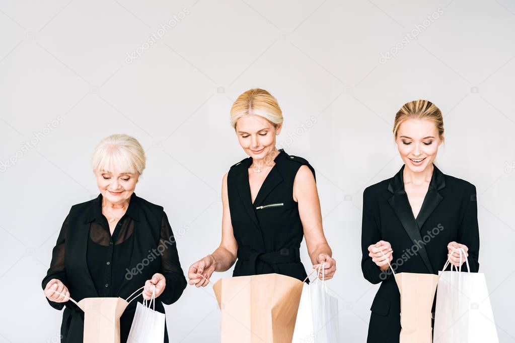 fashionable three-generation blonde women in total black outfits looking in shopping bags isolated on grey