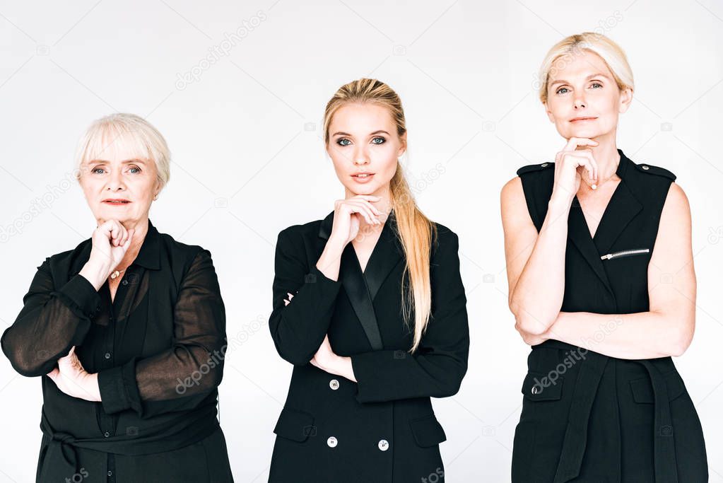 fashionable three-generation blonde women in total black outfits with hands near chins isolated on grey