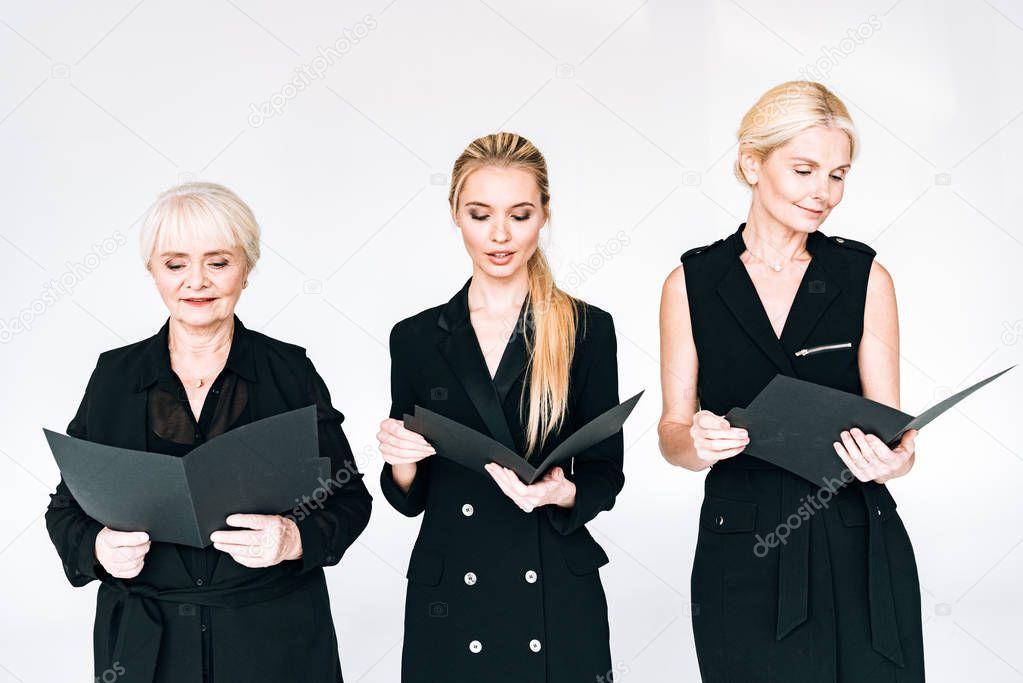 fashionable three-generation blonde businesswomen in total black outfits with folders isolated on grey