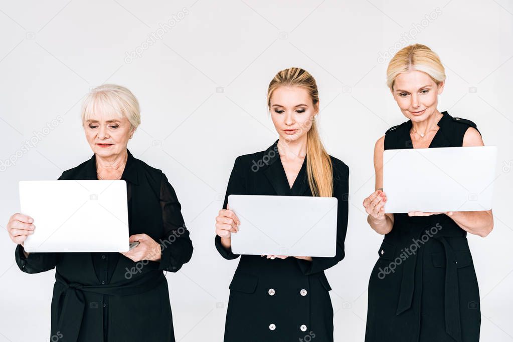 fashionable three-generation blonde businesswomen in total black outfits with laptops isolated on grey