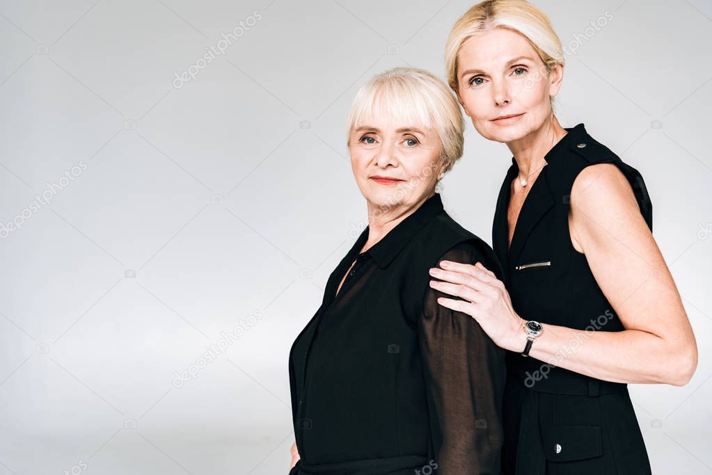 elegant blonde mature daughter and senior mother in total black outfits isolated on grey