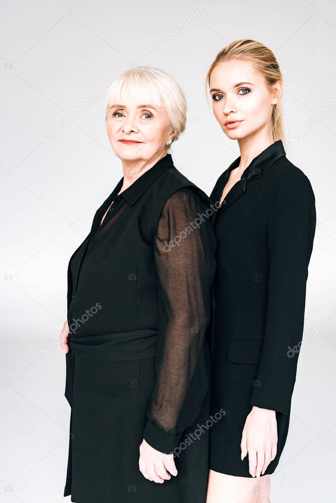 elegant blonde granddaughter and grandmother in total black outfits isolated on grey