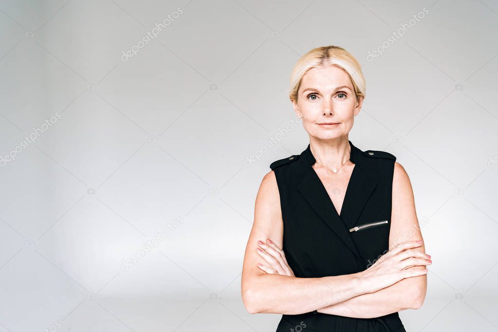elegant mature woman in black outfit with crossed arms isolated on grey