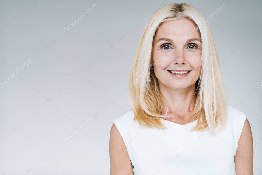 happy blonde mature woman smiling isolated on grey