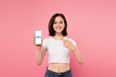 Kiev, Ukrayna - 3 Temmuz 2019: pembe izole skype logosu ile akıllı telefon parmak ile işaret gülümseyen kız