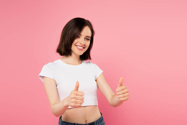 beautiful smiling girl showing thumbs up isolated on pink