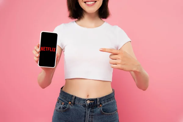 乌克兰 2019年7月3日 裁剪视图的女孩用手指指着智能手机与Netflix标志隔离在粉红色 — 图库照片
