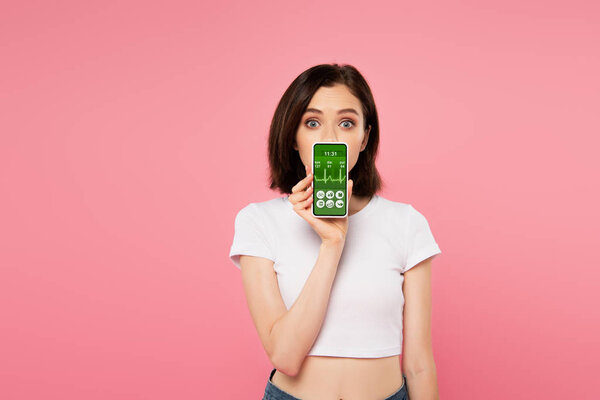 surprised girl holding smartphone with health tracking app isolated on pink