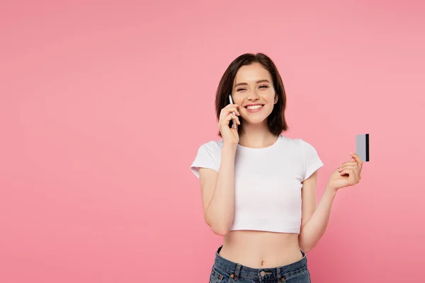 Chica Sonriente Sosteniendo Tarjeta Crédito Hablando Teléfono Inteligente Aislado Rosa — Foto de Stock