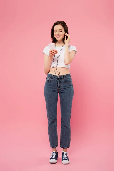 Pohled Usměvavou Dívku Naslouchající Hudbě Sluchátkách Smartphone Izolovaným Růžovém — Stock fotografie