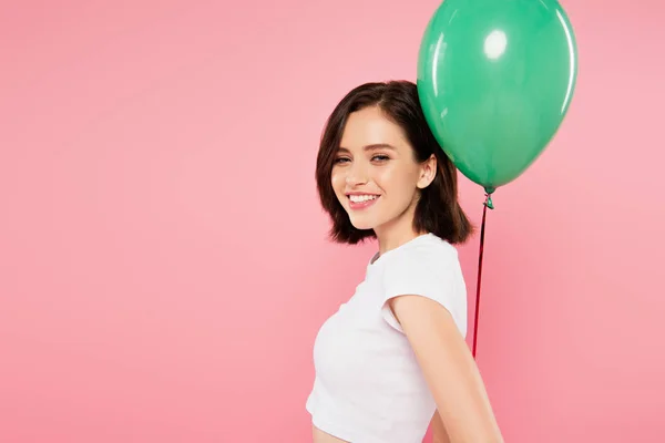 快乐微笑的漂亮女孩拿着绿色气球孤立在粉红色 — 图库照片