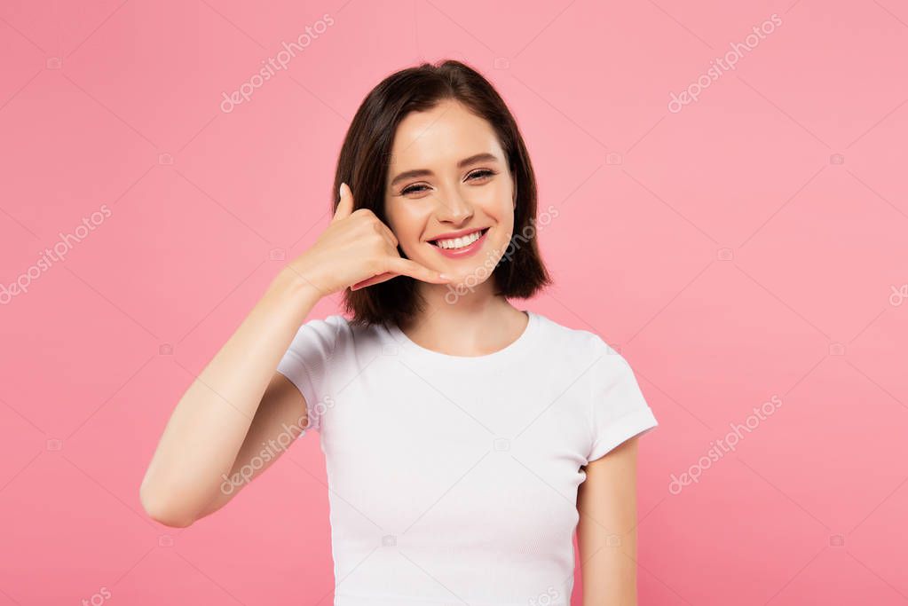 beautiful smiling girl showing call me gesture isolated on pink