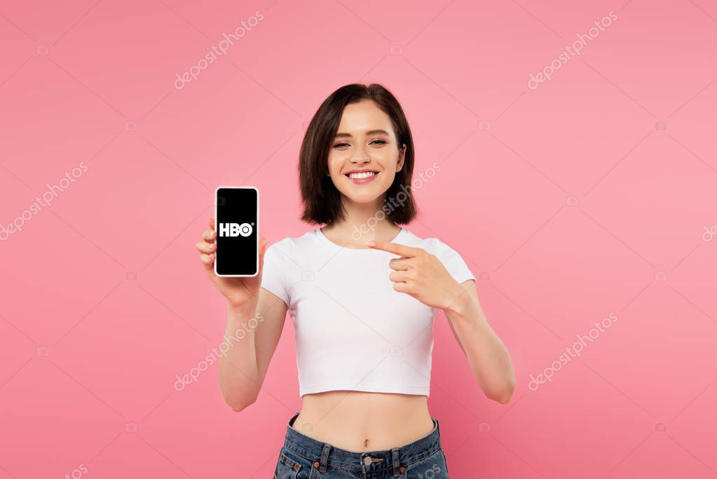 KYIV, UKRAINE - JULY 3, 2019: smiling girl pointing with finger at smartphone with HBO logo.