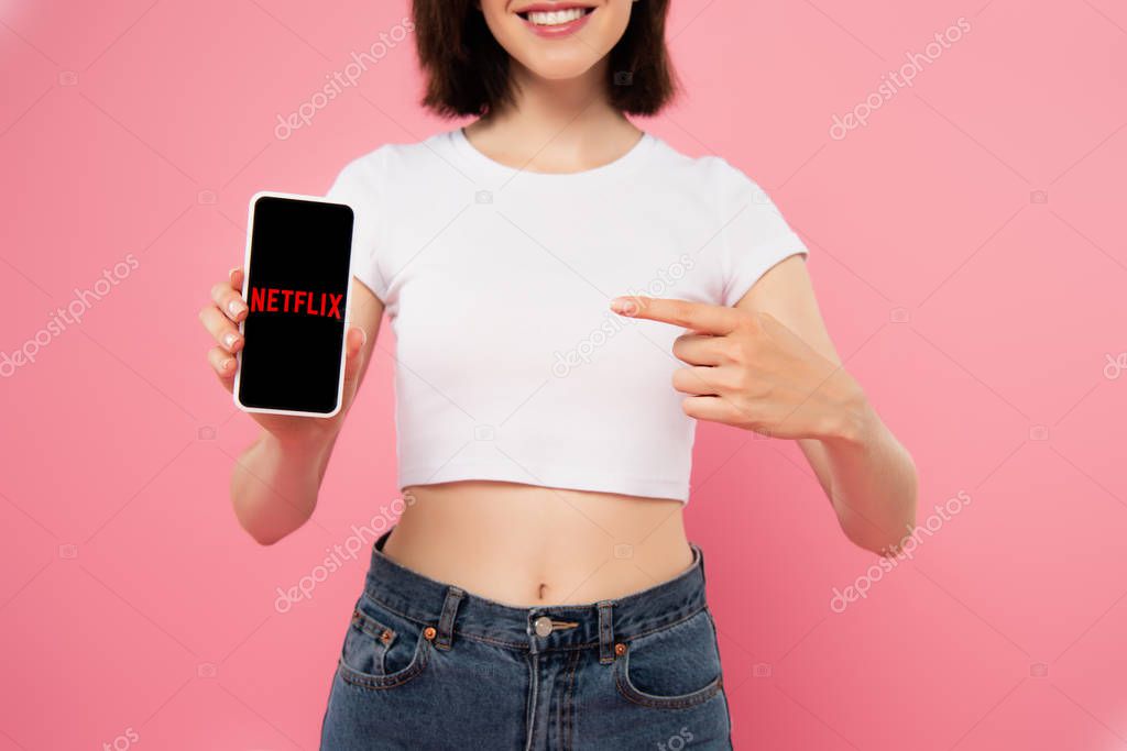 KYIV, UKRAINE - JULY 3, 2019: cropped view of girl pointing with finger at smartphone with netflix logo isolated on pink