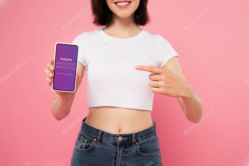 KYIV, UKRAINE - JULY 3, 2019: cropped view of girl pointing with finger at smartphone with Instagram logo isolated on pink