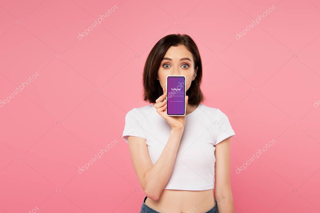 KYIV, UKRAINE - JULY 3, 2019: shocked girl holding smartphone with instagram logo isolated on pink
