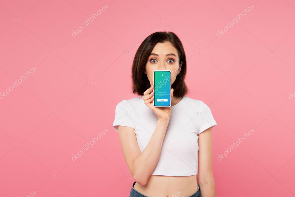 KYIV, UKRAINE - JULY 3, 2019: shocked girl holding smartphone with twitter logo isolated on pink