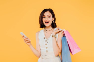 alışveriş çantaları ile heyecanlı moda kız sarı izole akıllı telefon konuşuyor