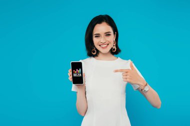 Kiev, Ukrayna - 3 Temmuz 2019: mavi üzerine izole deezer logosu ile akıllı telefon parmak ile işaret elbise gülümseyen zarif kadın