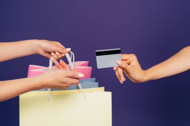 cropped view of women holding shopping bags and credit card isolated on purple clipart