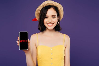 Kiev, Ukrayna - 3 Temmuz 2019: mor izole netflix uygulaması ile akıllı telefon tutan hasır şapka gülümseyen kız