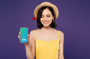 Kiev, Ukrayna - 3 Temmuz 2019: mor izole twitter uygulaması ile akıllı telefon tutan hasır şapka gülümseyen kız